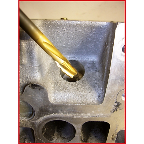 Nahaufnahme eines metallischen Lochs, das mit einem goldfarbenen Gewindeschneider bearbeitet wird.